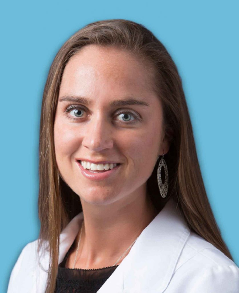 A professional headshot of a smiling woman in a white coat against a blue background.