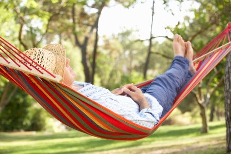 A person relaxing in a colorful hammock outdoors, wearing a straw hat and casual clothing