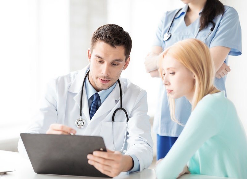 A doctor showing a patient information on a tablet while a nurse stands in the background.