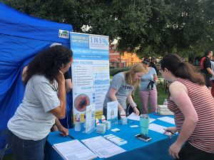 A skin cancer awareness booth at an outdoor event, with people engaging in educational materials.