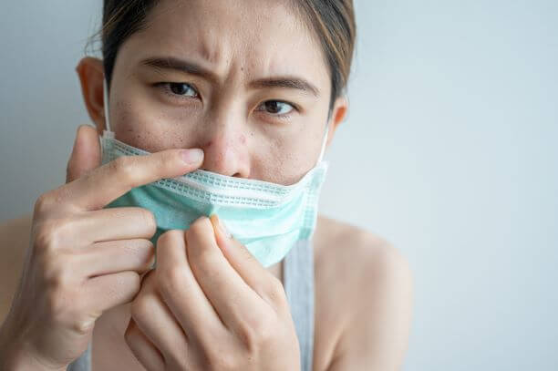 Woman examines maskne acne breakout on nose