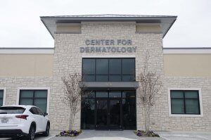 A dermatology center with a stone facade, large windows, and a parked white SUV outside