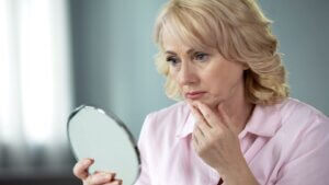 Woman looking in the mirror concerned with Ozempic Face