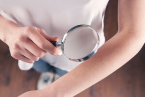 how to detect skin cancer - person looking at arm under magnifying glass