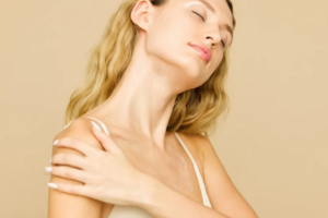A woman with glowing skin applying lotion to her shoulder, enjoying a self-care moment.